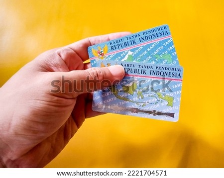 Two Indonesian identity cards (KTP) in human hand on a Yellow Background.