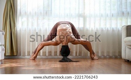Healthy fit Asian woman in sportswear practicing yoga at home,  in her living room. Wide leg forward fold pose D 