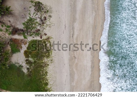 Drone shot of a man in the sand with sea on the right and trees on the left