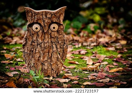  Gorgeous portrait picture of a owl, which is made up of wood. On a background is autumn leaves and green grass. 