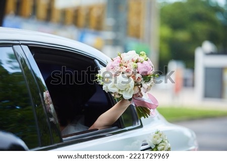 The bride's hand holding a bouquet outside the car window. Wedding ceremony and walk