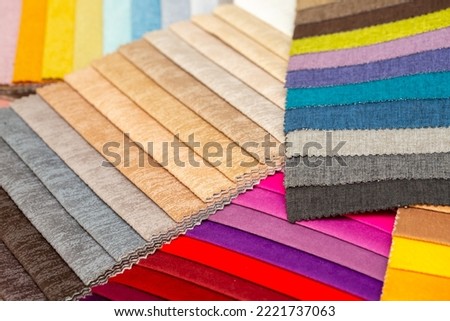 Fabric swatches in different colors are stacked for selection. A variety of shades of upholstery material for furniture and interior. Fabric texture close up. A set of multi-colored rolls of material.