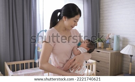 asian first time mom is singing lullaby quietly to her baby girl while cradling her in the arms during naptime inside a bedchamber. Royalty-Free Stock Photo #2221740621