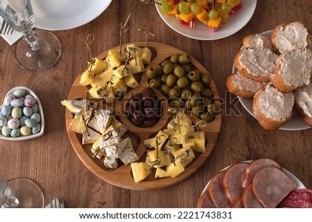 Cheese plate and other snacks on a wooden table. Assorted cheeses on a wooden rack. Cheese plate: camembert, brie cheese, olives and chocolate drops. Top view.  Royalty-Free Stock Photo #2221743831