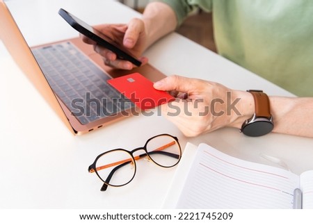 A man holds a bank card in his hands while sitting in his kitchen. The concept of budget planning, payment for online purchases. High quality photo