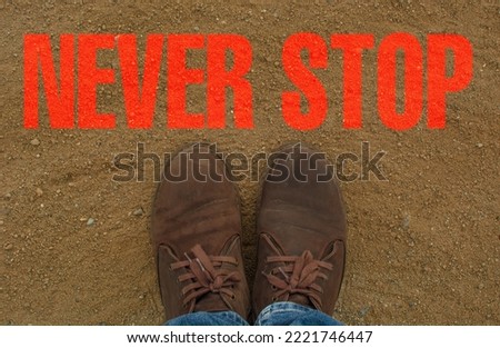 The brown suede shoes are on an earthen floor, with the writing never stop on the floor.
