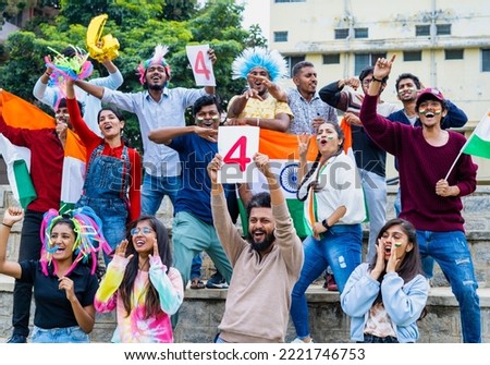 Group of people with four sign board and indian flags shouting and celebrating the boundary while watching cricket match at stadium - concept of excitement, enjoyment and cheerful indian crowd.