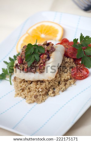 Baked halibut with olive tapenade crust garnished with couscous, fried cherry tomatoes, and fresh parsley. 