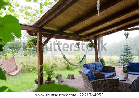Beautiful covered terrace in the green garden with natural wood, rattan furniture, hammock. Summer outdoor and relax in patio. Royalty-Free Stock Photo #2221764955