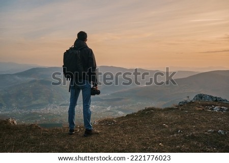 A male traveler photographer on the mountain top during the hike at sunrise or sunset.	