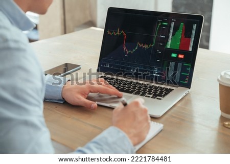 Picture with no face and rare view of male hands scrolling diagram of crypto currency market on his laptop, making notes, creating new strategy of successful development, avoiding high risks