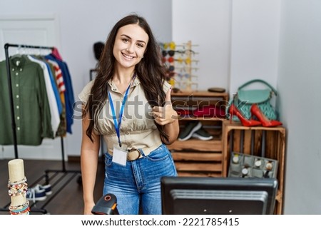 Young brunette woman working as manager at retail boutique smiling happy and positive, thumb up doing excellent and approval sign 