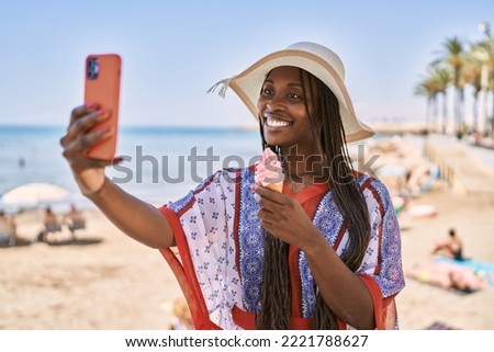 Young african american woman eating ice cream and make selfie by the smartphone at the beach.
