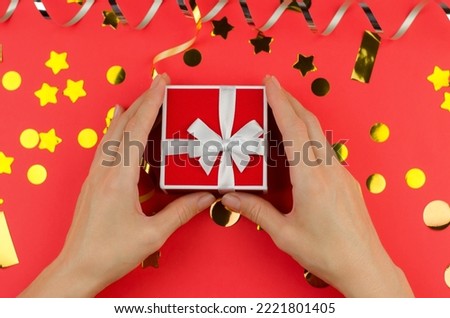 Red gift box in female hands on a red festive background