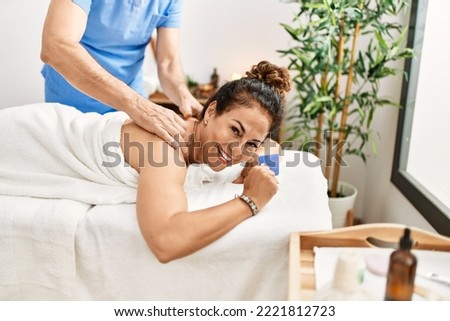 Middle age man and woman wearing therapist uniform having back massage session and holding credit card at beauty center