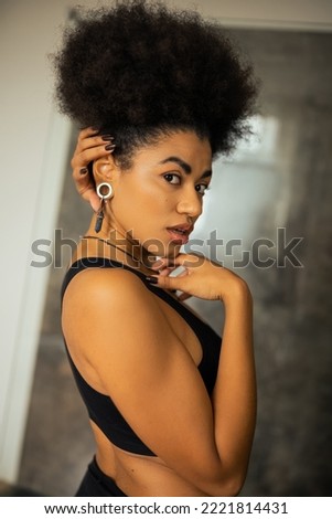 Portrait of young african american woman in crop top looking at camera in blurred bathroom