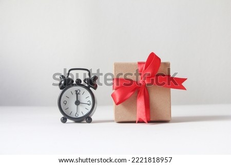 Gift box with black alarm clock on white background.