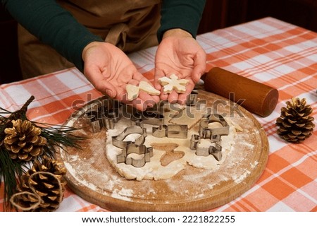 Carved snowflake and angel wings made of ginger dough in the hands of a housewife, pastry chef, preparing gingerbread cookies for Christmas. On the table are golden pine cones on the fir-tree branch