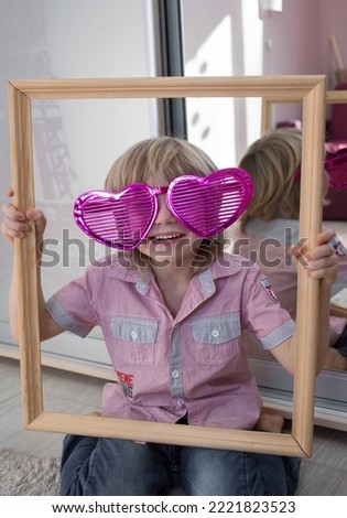 cute caucasian boy in a huge pink funny heart-shaped glasses is holding a big frame. Valentine's Day, a holiday for all lovers. congratulations for loved ones