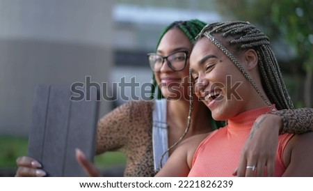Two young black women taking selfie with tablet. African American girlfriends with braided hairstyle holding device outdoors 2
