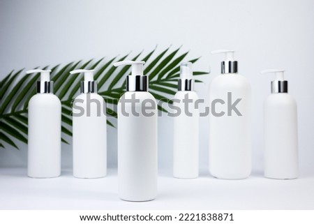 Set of white cosmetic bottles mockup with palm leaf. White plastic bottles with shampoo and conditioner and shower gel on a white background. Mockup cosmetic bottle on white background