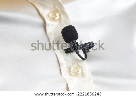 The lavalier microphone is secured with a clip on a women shirt close-up. Audio recording of the sound of the voice on a condenser microphone