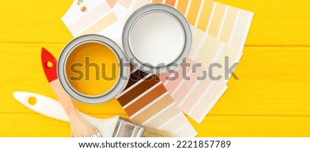 Cans of paints, brushes and color patterns on yellow wooden background