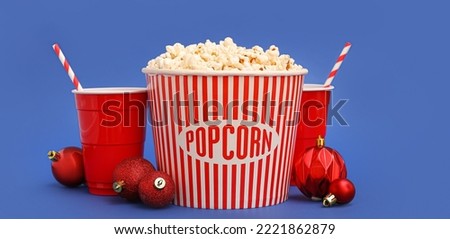 Bucket of popcorn, cups of soda drink and Christmas balls on blue background