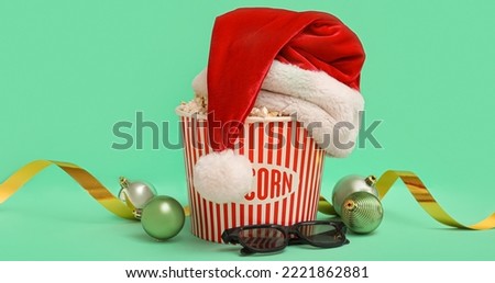 Bucket of popcorn with Santa hat, 3D glasses and Christmas balls on green background