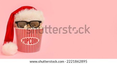 Bucket of popcorn with Santa hat and 3D glasses on pink background with space for text