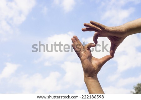 man hands forming a heart over the blue sky