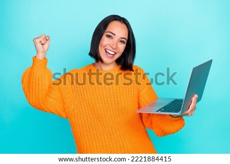 Photo of funny lucky girl dressed orange pullover winning game modern gadget rising fist isolated teal color background Royalty-Free Stock Photo #2221884415