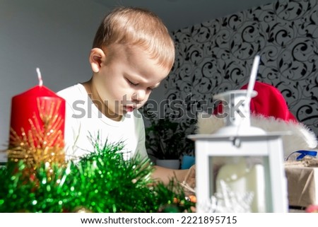 A small child with Christmas gifts is sitting at a New Year's wooden table with a tablet in his hands. Celebrating Christmas.
