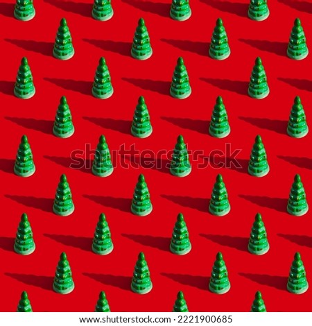 Repeating pattern from a green toy Christmas tree with a shadow on a red background.The concept of the New Year and Christmas.
