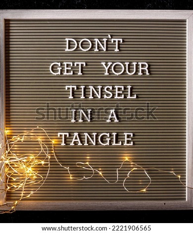 Don't get your tinsel in a tangle quote on a letter board with a tangled strand of warm glowing mini lights