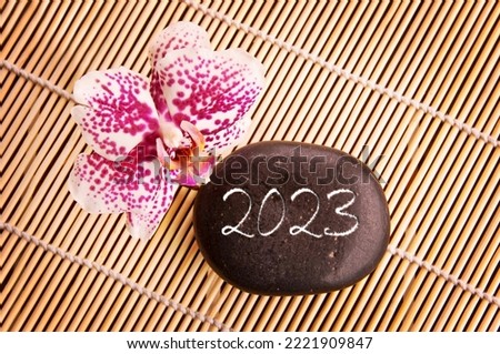 2023 written on a black stone with pink orchid, zen greeting card