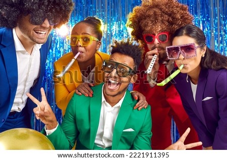 Happy cheerful joyful smiling multiracial people wearing different bright yellow green red blue purple costumes, funny disco glasses, crazy curly wigs blow party horns on festive photobooth background Royalty-Free Stock Photo #2221911395
