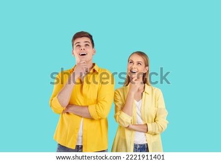 Young couple making holiday plans. Happy man and woman in casual yellow shirts standing isolated on turquoise background, looking up, holding hands on chins, thinking about something nice and smiling