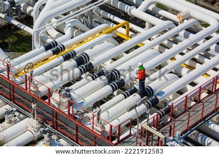 Top view male worker inspection at steel long pipes and pipe elbow valve in station oil factory during refinery valve of visual check record pipeline oil and gas industry. Royalty-Free Stock Photo #2221912583