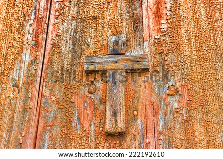 A brownish wooden Catholic cross nailed on grungy orange old wall