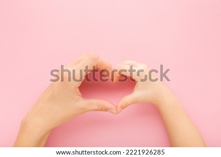 Heart shape created from little daughter and young mother hands on light pink table background. Pastel color. Lovely emotional, sentimental moment. Love, happiness and safety concept. Closeup.