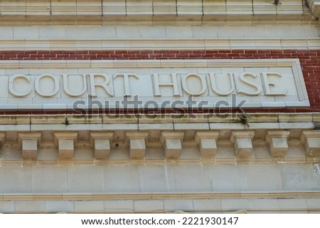 The exterior of a historical red brick judicial building with a limestone block and decorative marble wall.  The letters courthouse or court house in the capital text is embossed on the molding. 