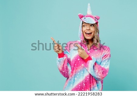 Young happy woman 20s wear domestic costume with hoody and animals ears point finger aside indicate on workspace mock up isolated on plain pastel light blue cyan background. People lifestyle concept