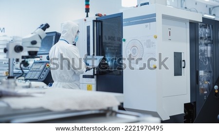 Heavy Industry Manufacturing Factory: Engineer in Sterile Coverall Working on Laptop Computer, Examining Industrial CNC Machine Setting and Configuring Functionality.
