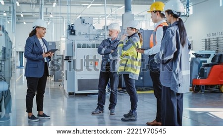Factory Meeting: Black Female Chief Engineer Talking to Colleagues Before Work Day in Heavy Industry Manufacturing Facility. Diverse Group of Employees Listening to Manager. Royalty-Free Stock Photo #2221970545