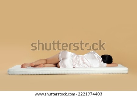 Young woman lying on soft mattress against beige background, back view Royalty-Free Stock Photo #2221974403
