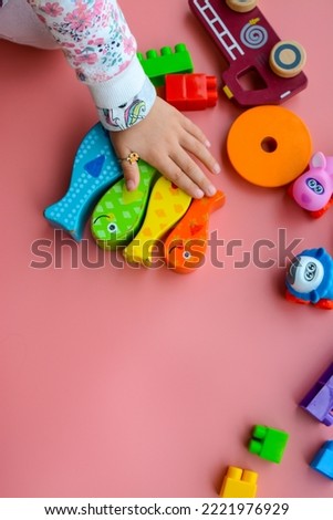 Kid hands playing with colorful toys on pink background