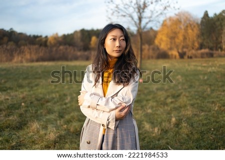 Middle aged Asian woman in coat looking away walking in Autumn forest