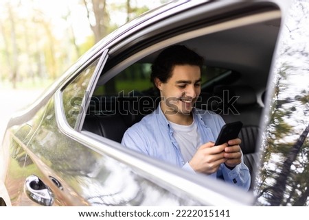 Happy smiling business man typing message on phone while sitting in a taxi. Young businessman in formal clothing using smartphone while sitting on back seat in car. Cheerful guy messaging with cell. Royalty-Free Stock Photo #2222015141