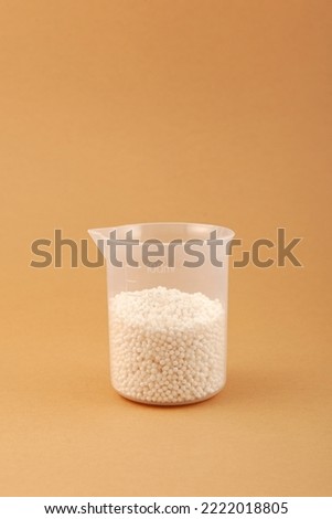 Chemical fertilizer in plastic measuring cup. Small white balls. Agricultural economics. Test fertilizer for peasant farm.